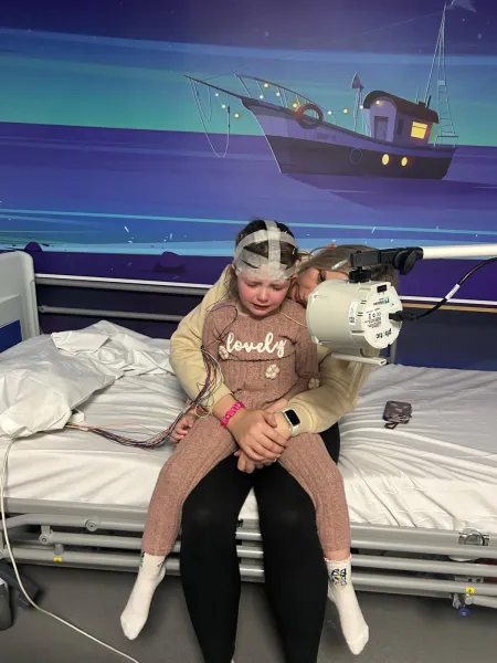 Young girl sitting on mother's lap ready for a scan looking upset