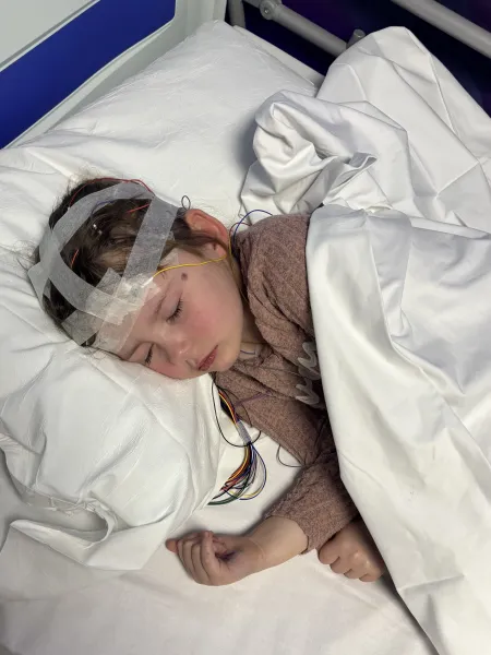 A young girl, Lilly, lies in a hospital bed with bandages on her head.