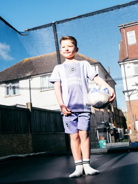 A young boy stands on a trampoline holding a football. 