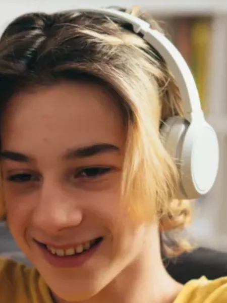 A boy wearing headphones smiles towards a laptop screen.