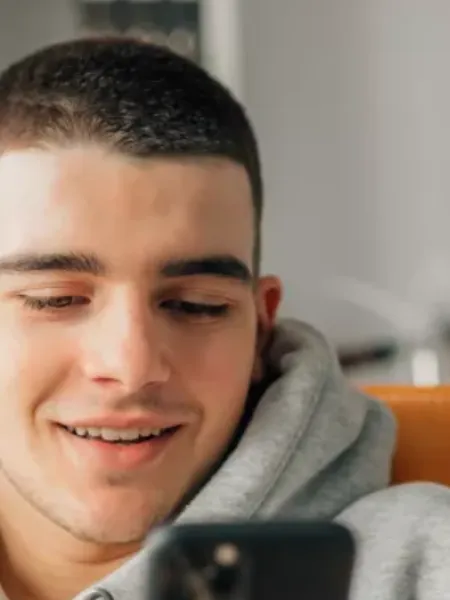 A young man smiles at his phone.