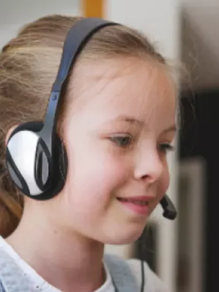 A young girl in headphones smiles on an online conversation.