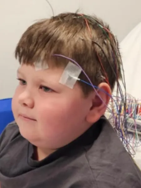A boy sits in a hospital bed with an EEG.