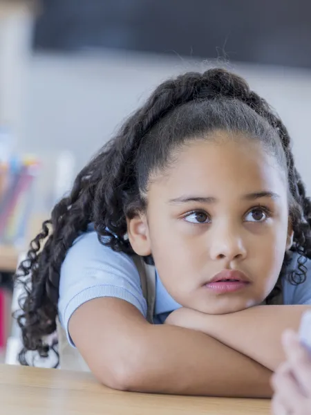 A young girl sits thoughtfully at a desk.