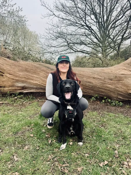 A young woman kneels next to her dog by a fallen tree.