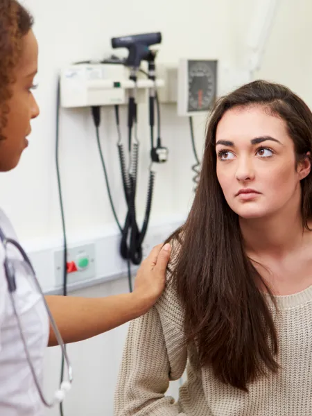 A young woman is speaking with a health professional at hospital, looking concerned.