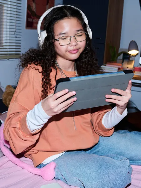 A teenage girl uses a tablet while wearing headphones.