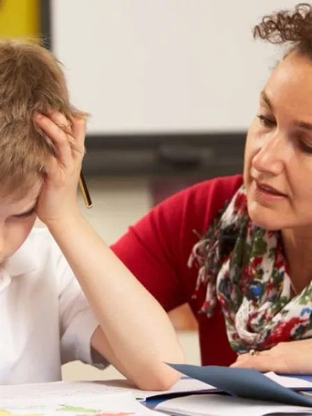 An educator speaks gently to a young student, who is holding his hair in frustration.