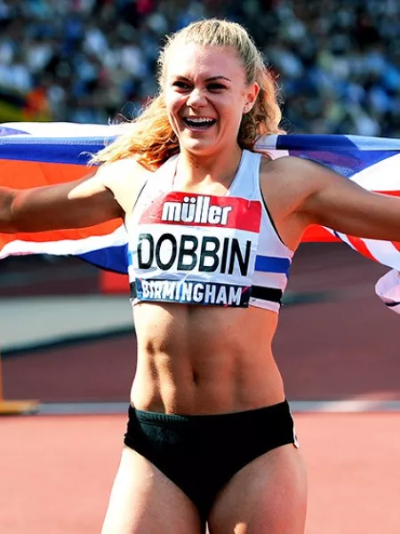 Olympian Beth Dobbin holds a Union Jack flag behind her after completing a race, smiling widely.