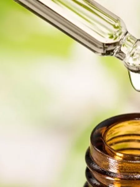 CBD oil drips from a pipette into a medicinal bottle.