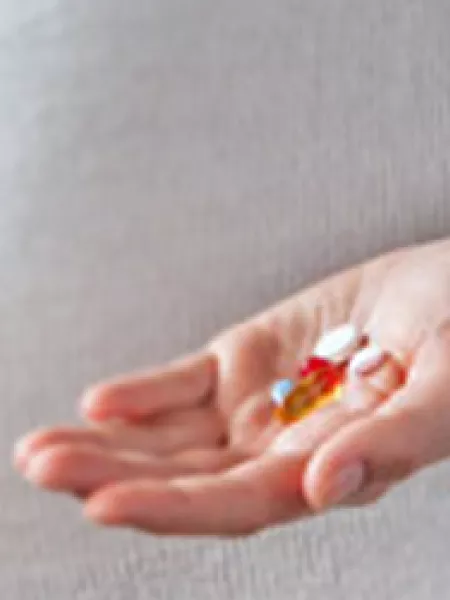 An expecting woman holds a handful of sodium valproate tablets in front of her pregnant belly.